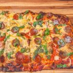 Pizza in teglia appena sfornata, con bordo dorato e topping ricco, su un piano di lavoro.