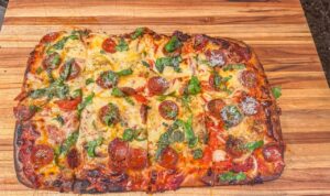 Pizza in teglia appena sfornata, con bordo dorato e topping ricco, su un piano di lavoro.