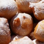Frittelle veneziane dorate e spolverate di zucchero, servite su un piatto elegante.