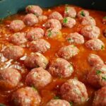 Polpette al sugo in un piatto, pronte per essere servite, con pomodoro fresco e basilico.