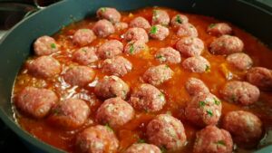 Polpette al sugo in un piatto, pronte per essere servite, con pomodoro fresco e basilico.