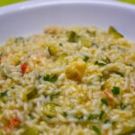 Risotto alla milanese cremoso, con zafferano e guarnizione di parmigiano, servito in un piatto bianco.