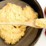Torta di mele soffice con una fetta tagliata, decorata con zucchero a velo su un piatto bianco.
